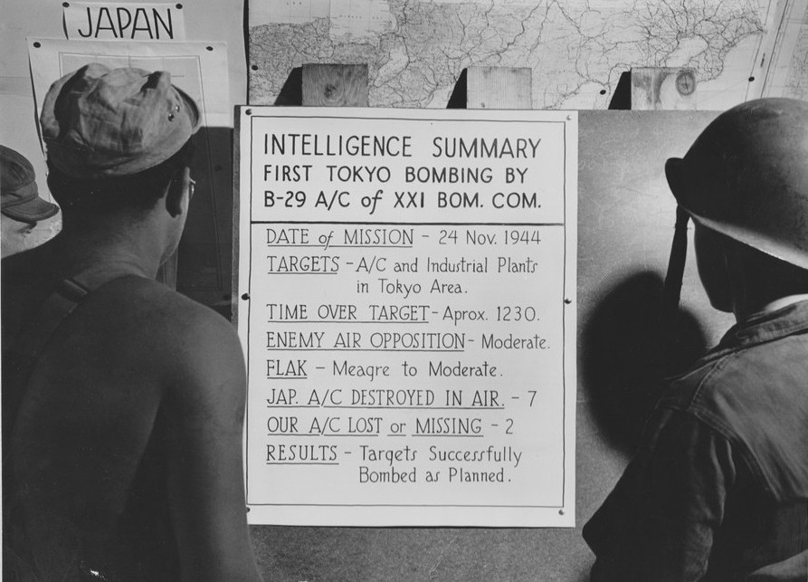 US airmen reading a bulletin announcing their Saipan, Mariana Islands-based unit's first bombing on Tokyo, Japan, late Nov 1944