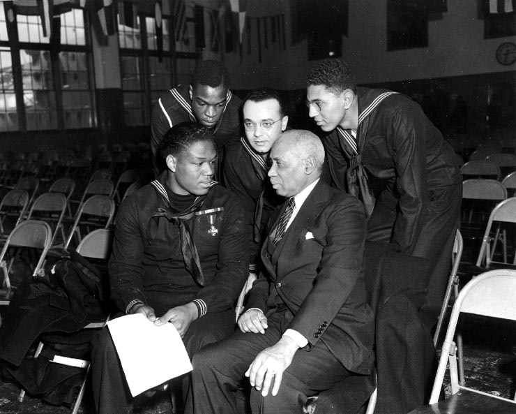 US Navy Mess Attendant First Class Doris Miller talking with three sailors and a civilian, during his war bond tour stop at the Naval Training Station, Great Lakes, Illinois, United States, 7 Jan 1943