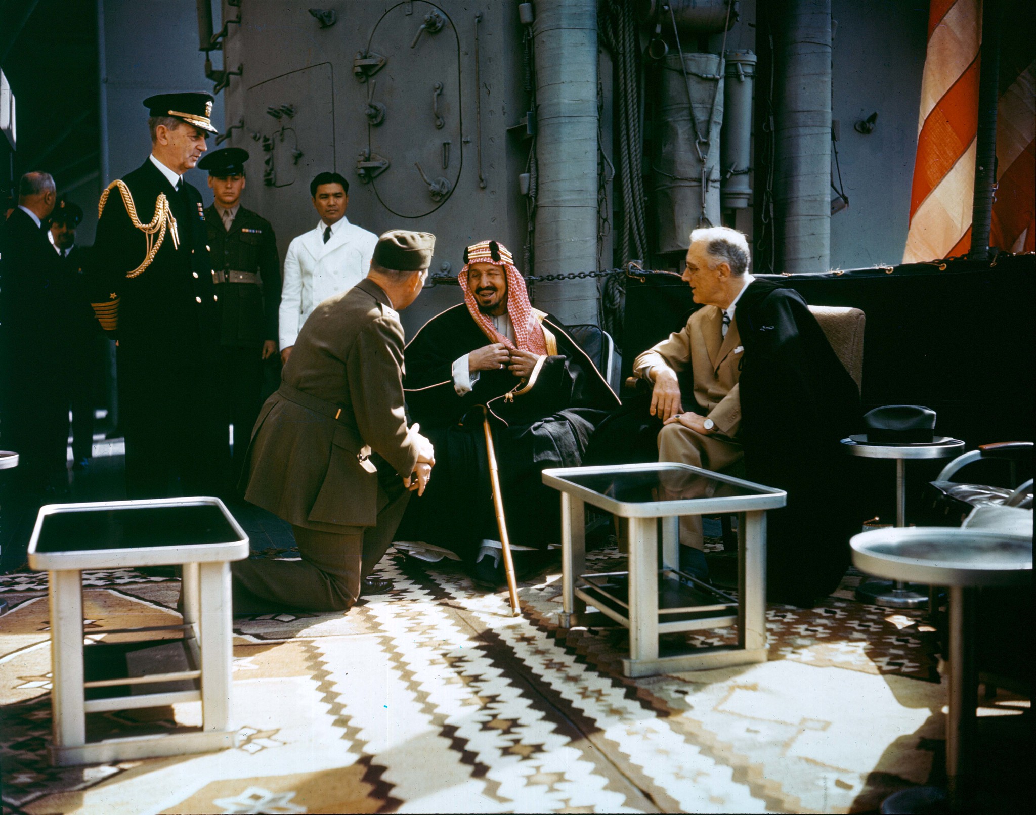 Franklin Roosevelt and King Abdul-Aziz (Ibn Saud) of Saudi Arabia aboard USS Quincy, Great Bitter Lake, Egypt, 14 Feb 1945. The King is speaking to the interpreter, Marine Corps Colonel William A. Eddy (kneeling), minister to Saudi Arabia