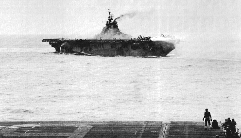 USS Hancock burning after being struck by special attack aircraft, off Okinawa, Japan, 7 Apr 1945; note USS Essex's flight deck in foreground