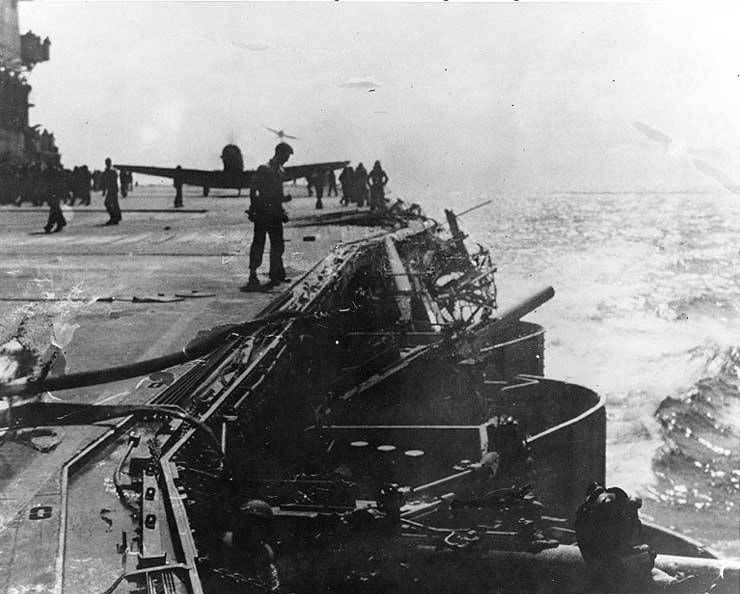 Damage to Lexington port side number six 5-in gun by dive bomb, Battle of Coral Sea, 8 May 1942, photo 2 of 2; note TBD-1 Devastator bomber on deck and F4F-3 Wildcat fighter approaching to land