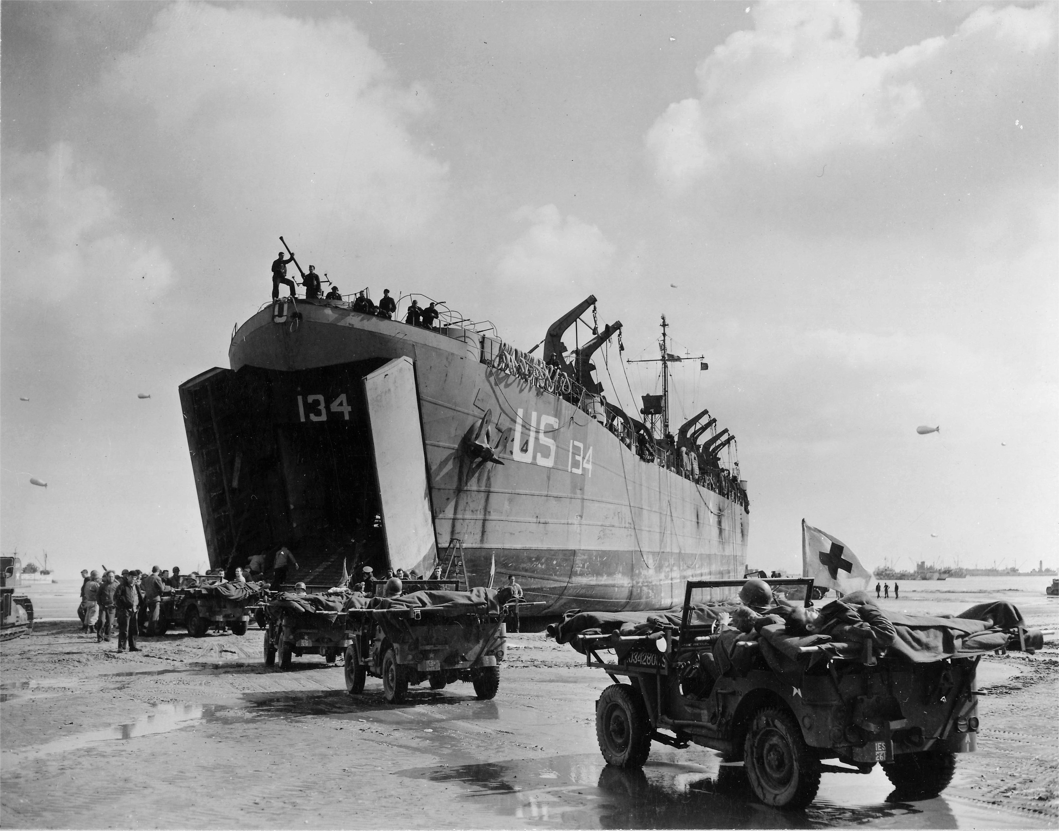 US Navy LST-134 and LST-325 beached at Normandy, France as jeeps driving along the invasion beach carry casualties to the waiting vessels, 12 Jun 1944, photo 2 of 4
