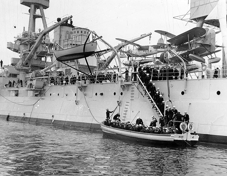 Midshipmen and sailors boarding a 50-foot motor launch from New York, during the summer 1940 US Naval Academy Midshipmen's cruise; note SOC-3 Seagull floatplanes of Observation Squadron Five onboard