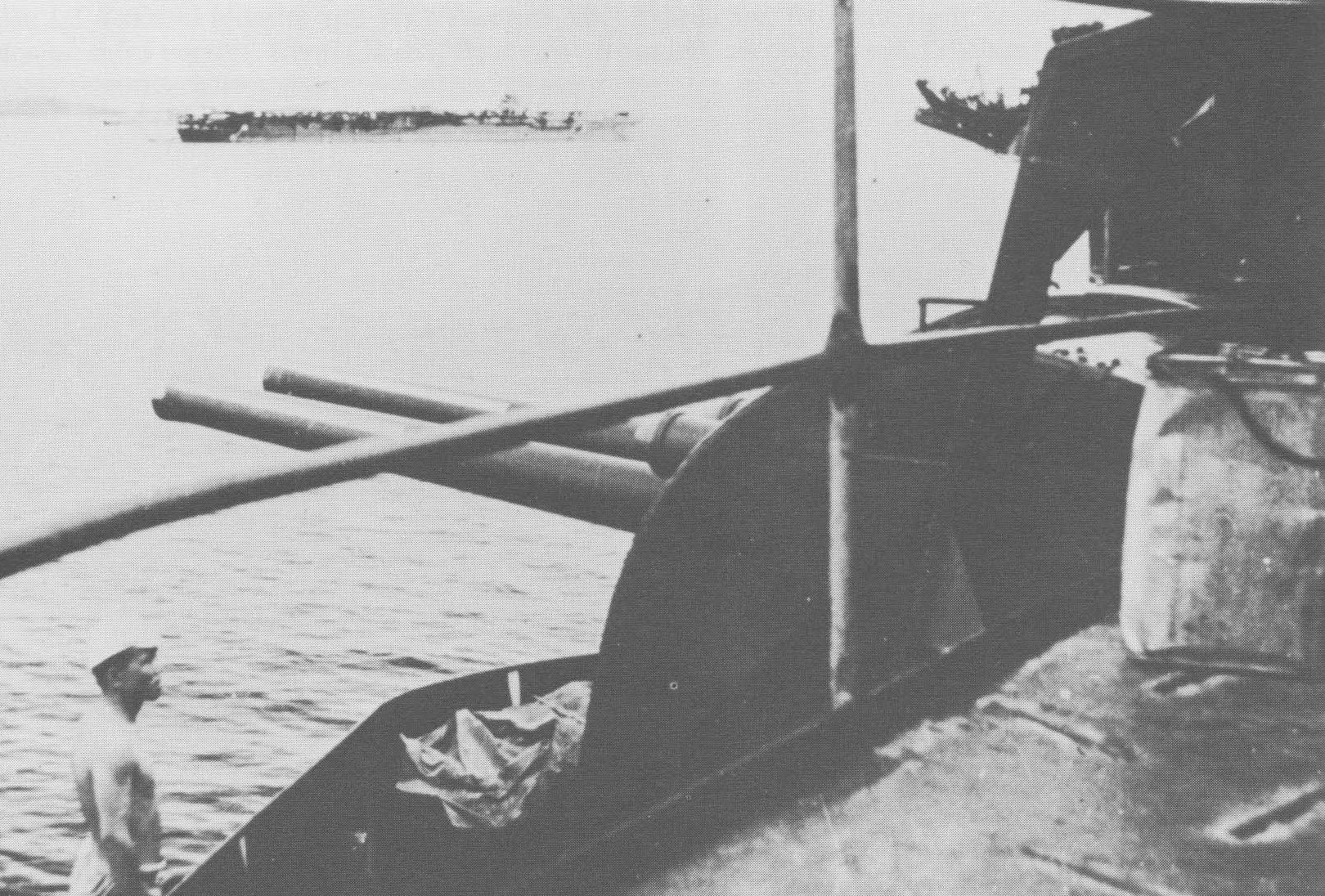 A sailor inspecting combat damage to anti-aircraft guns aboard either Shokaku, Zuikaku, 1942; the carrier in the background was either Shokaku or Zuikaku