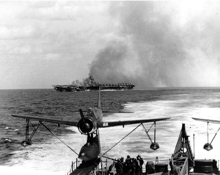 Carrier Ticonderoga burning after being struck by special attack aircraft off Taiwan, 21 Jan 1945; note light cruiser Miami's starboard catapult and OS2U Kingfisher aircraft in foreground