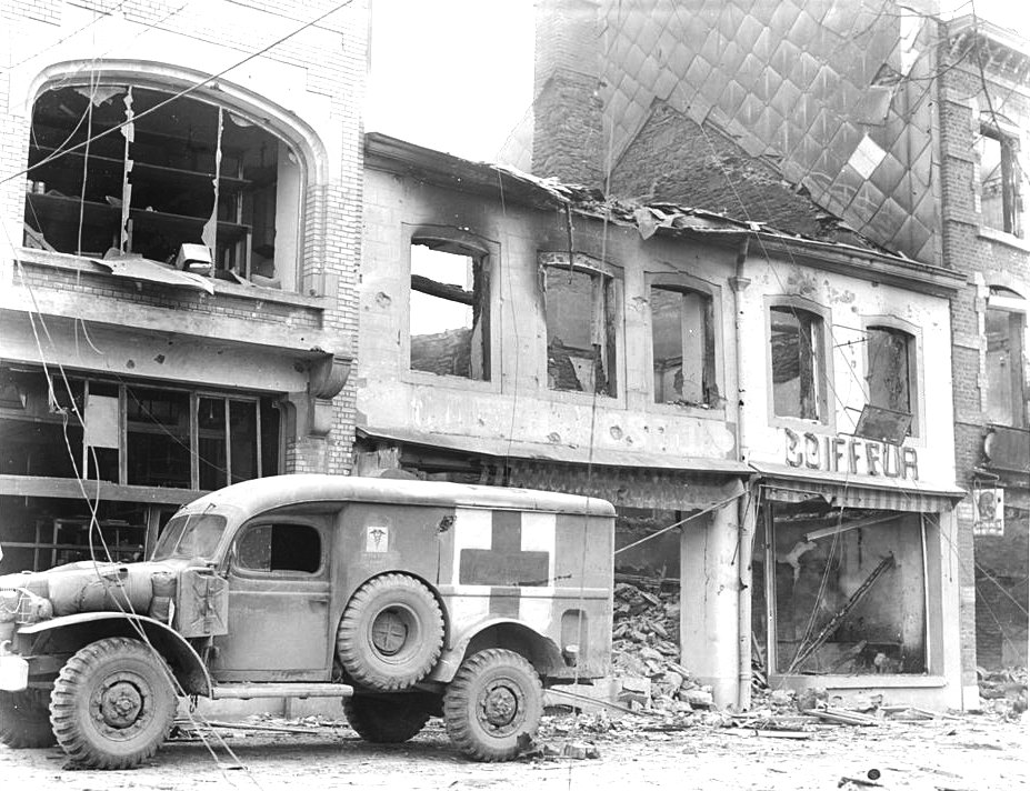 American ambulance waiting outside a bombed building in Bastogne, Belgium while a searcher looked for persons injured during the ten-day defense by US 101st Airborne Division, 26 Dec 1944
